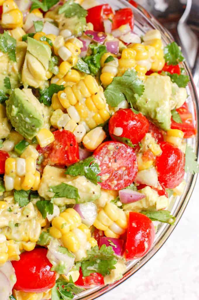 corn and avocado and cilantro and tomatoes in a bowl