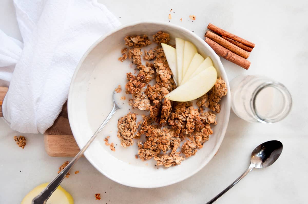 granola in a white bowl with milk and apple slices