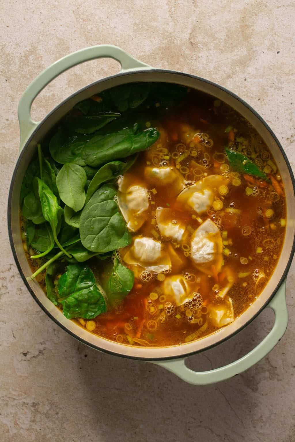 adding spinach and frozen wontons to dutch oven
