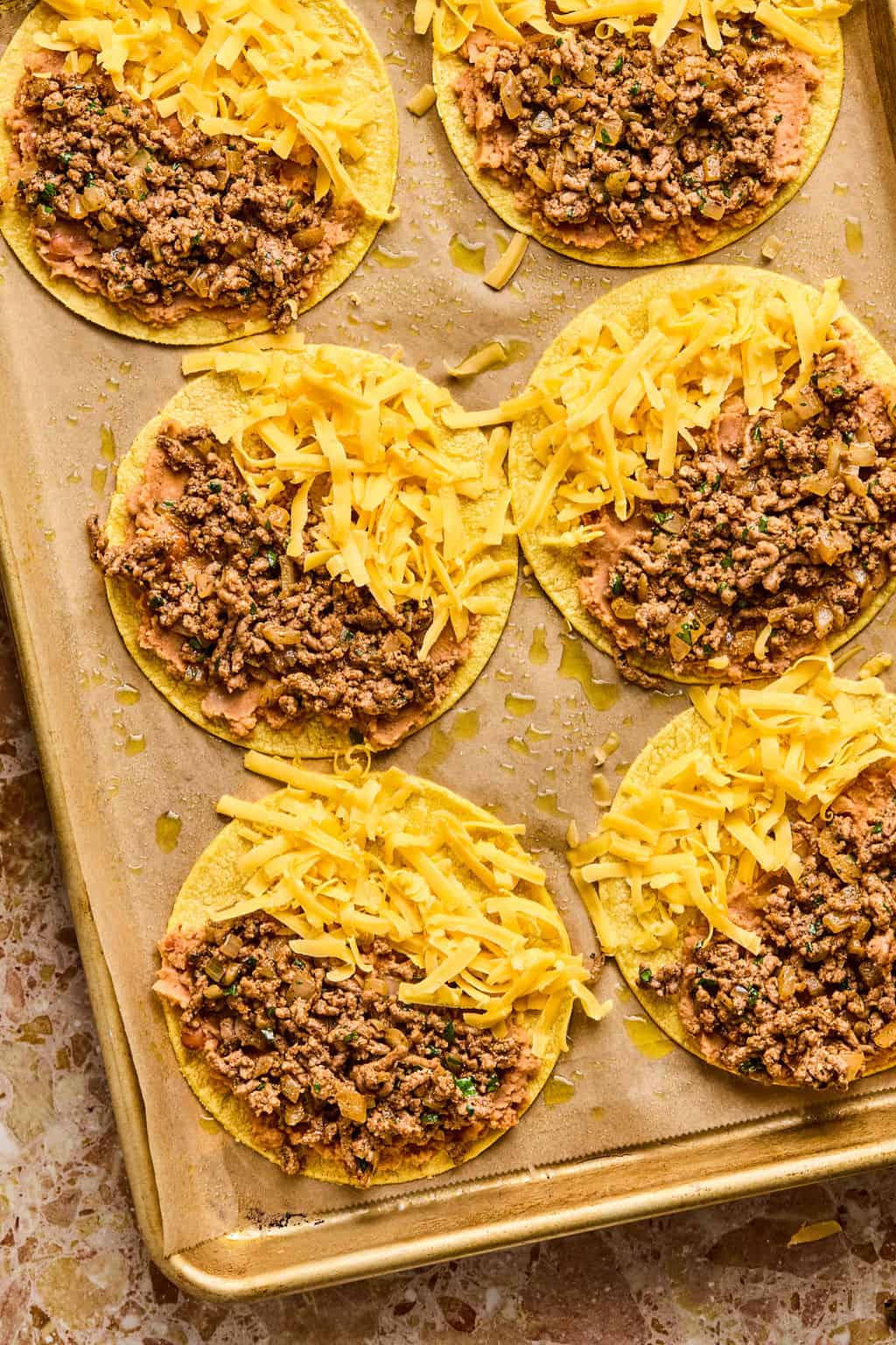 tortillas with refried beans, taco meat and cheese on them on baking sheets