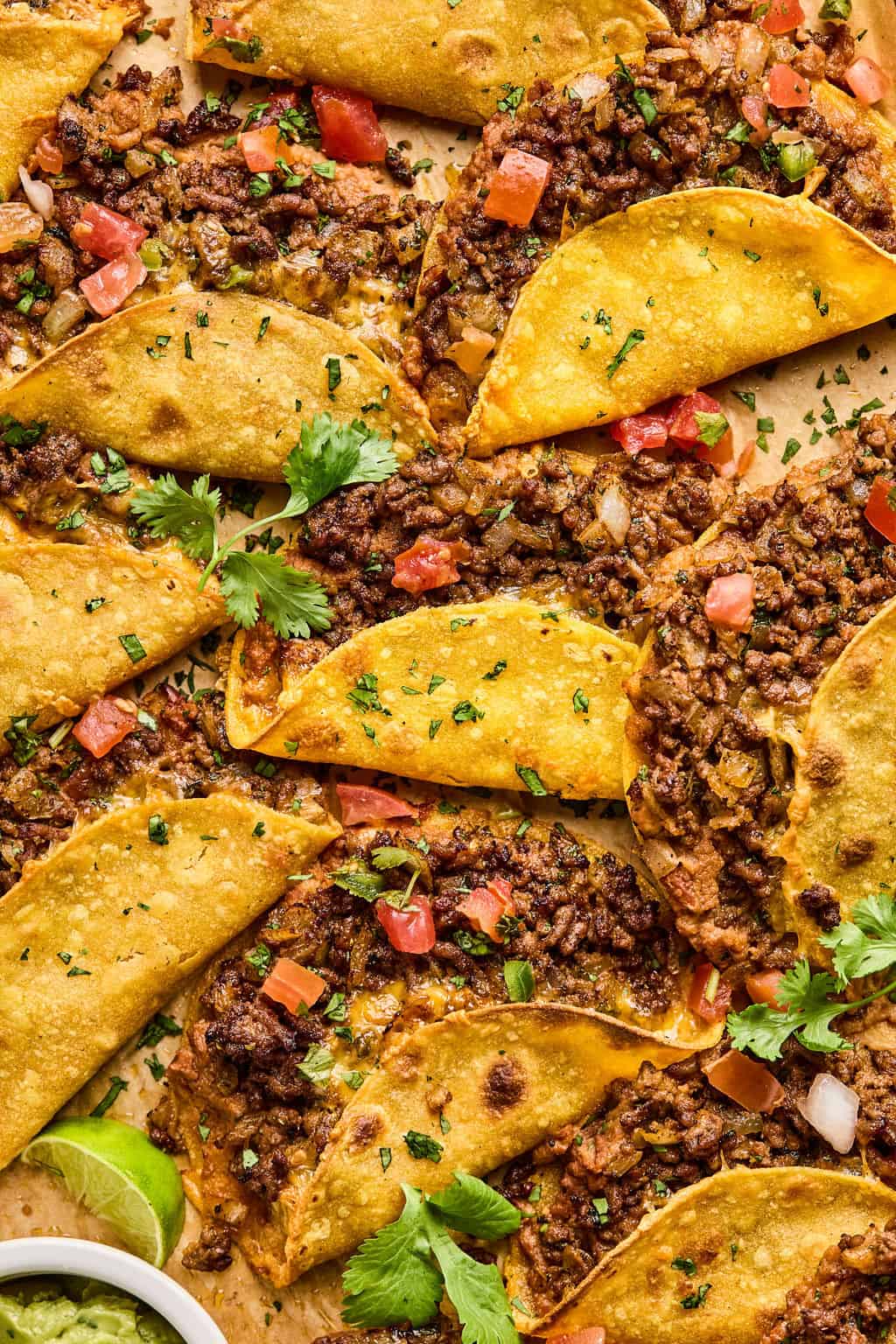 oven baked beef tacos on baking sheet with tomatoes and cilantro.