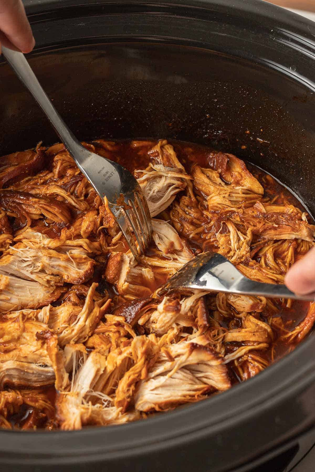 shredding chicken with two forks in the slow cooker