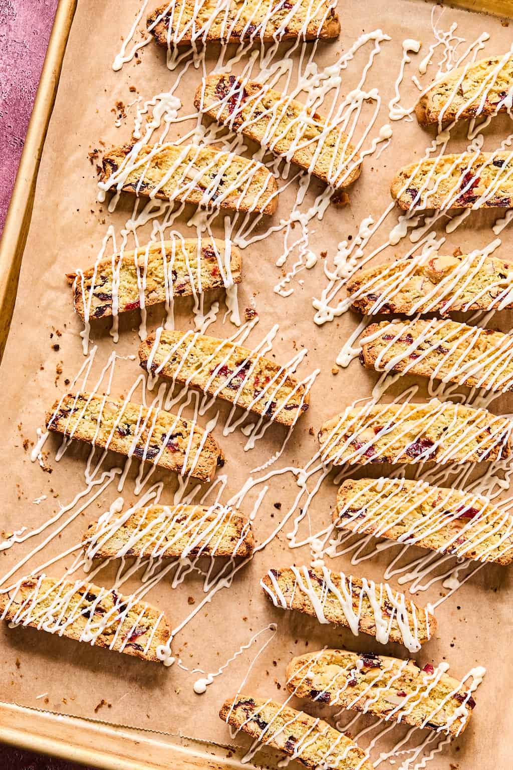 Almond Cranberry Biscotti on baking sheet with white chocolate drizzled on