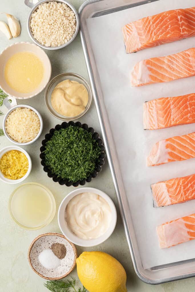salmon fillets on a parchment lined baking sheet, with recipe ingredients nearby 