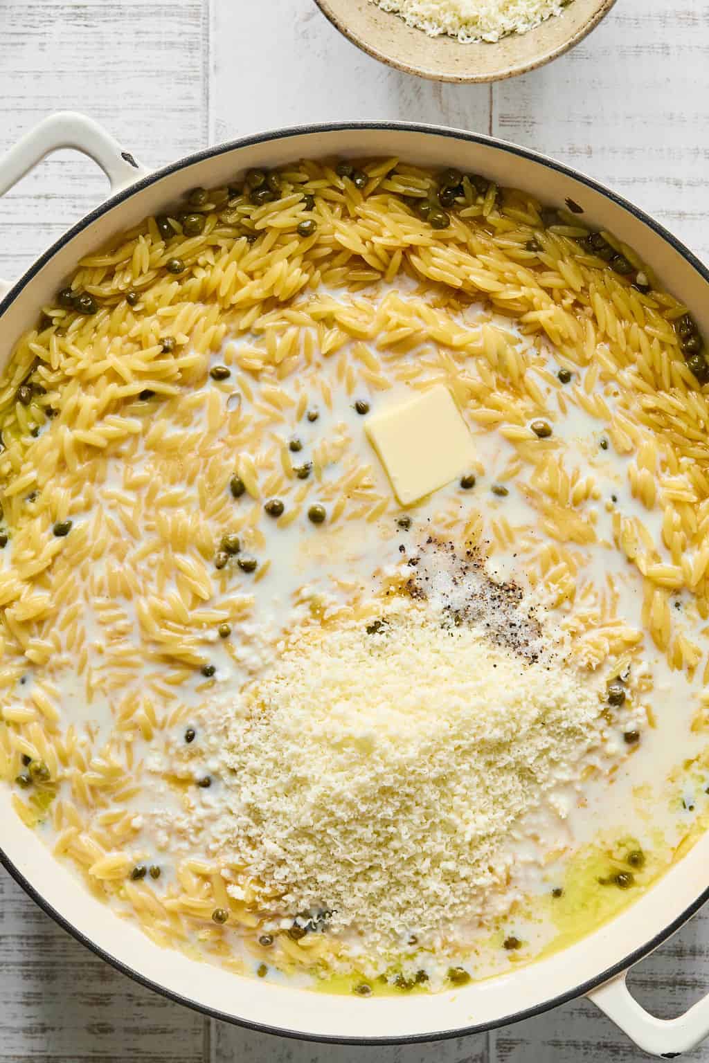 Adding butter, milk, pecorino romano, salt, and pepper to pan