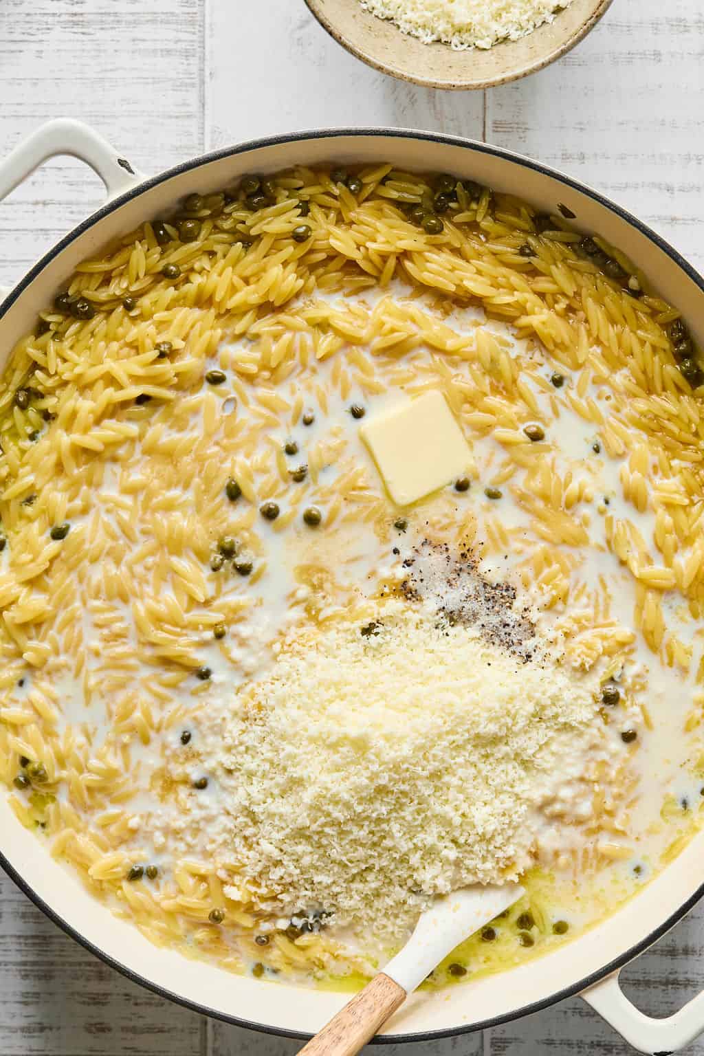 Adding butter, milk, pecorino romano, salt, and pepper to pan