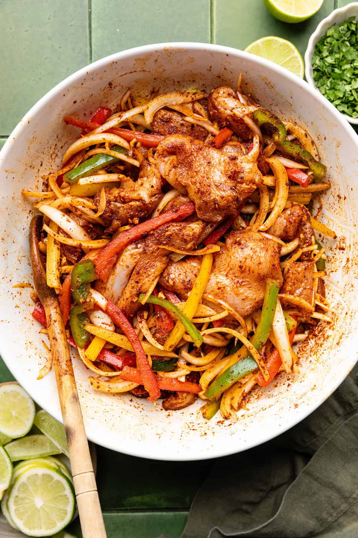 chicken, peppers, onions all marinating in fajita seasoning in a bowl