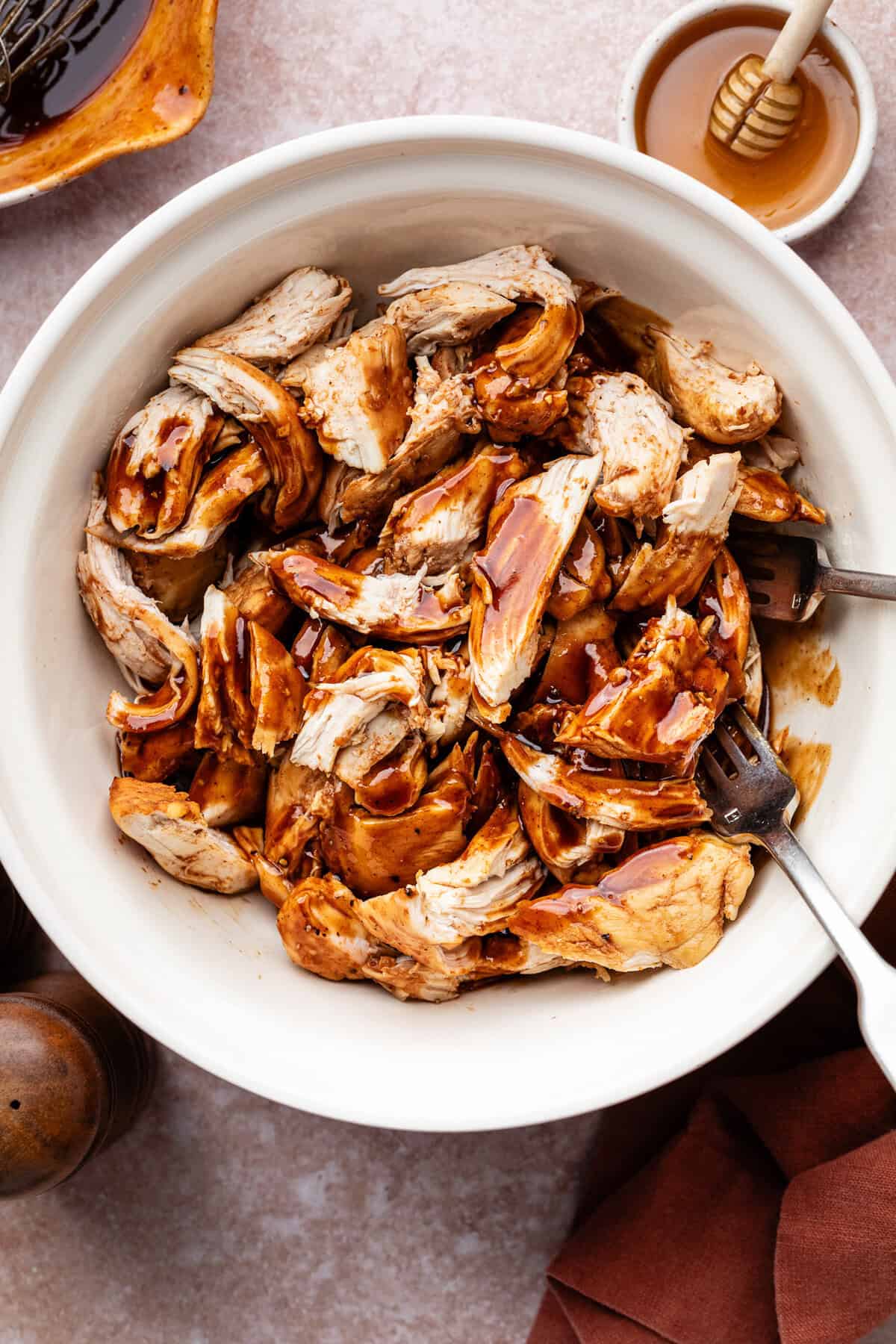 Shredded chicken breasts in white bowl with forks.