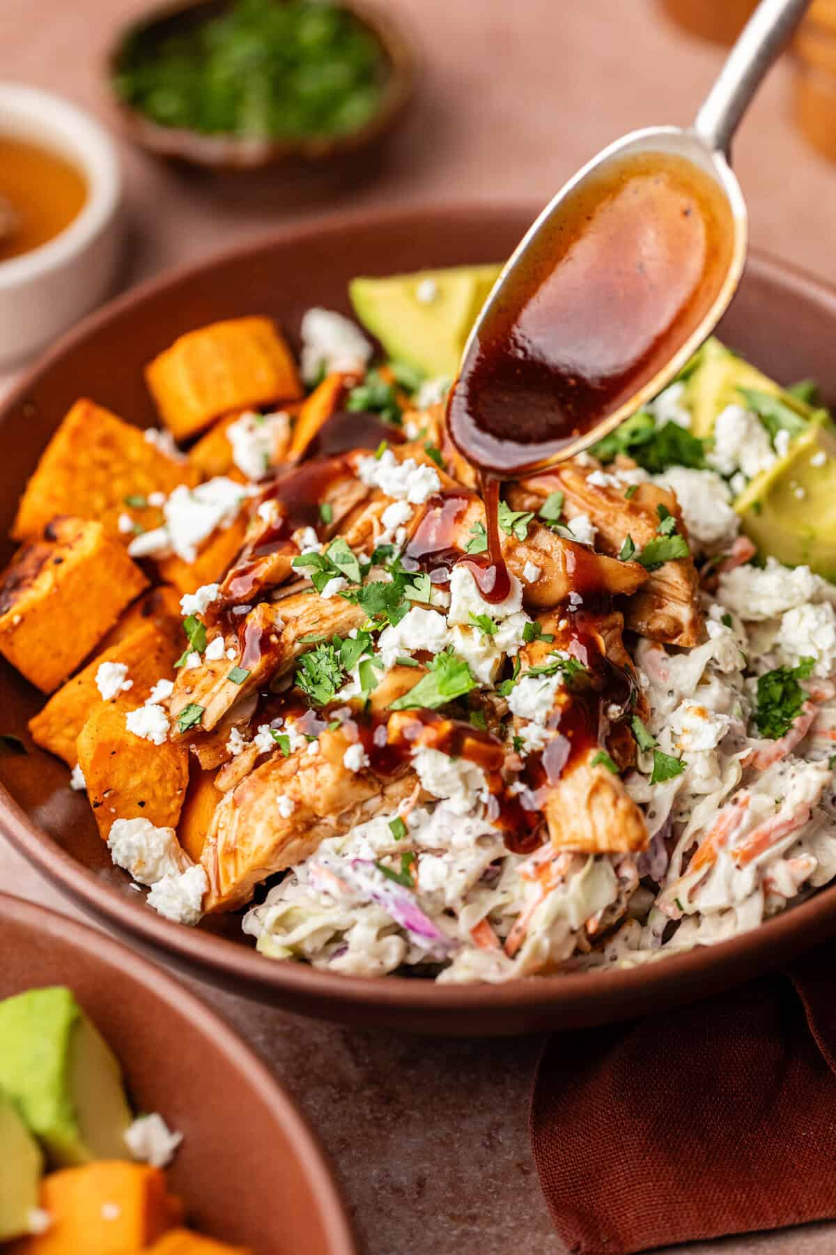 Pouring BBQ sauce on BBQ Chicken Sweet Potato Bowls.
