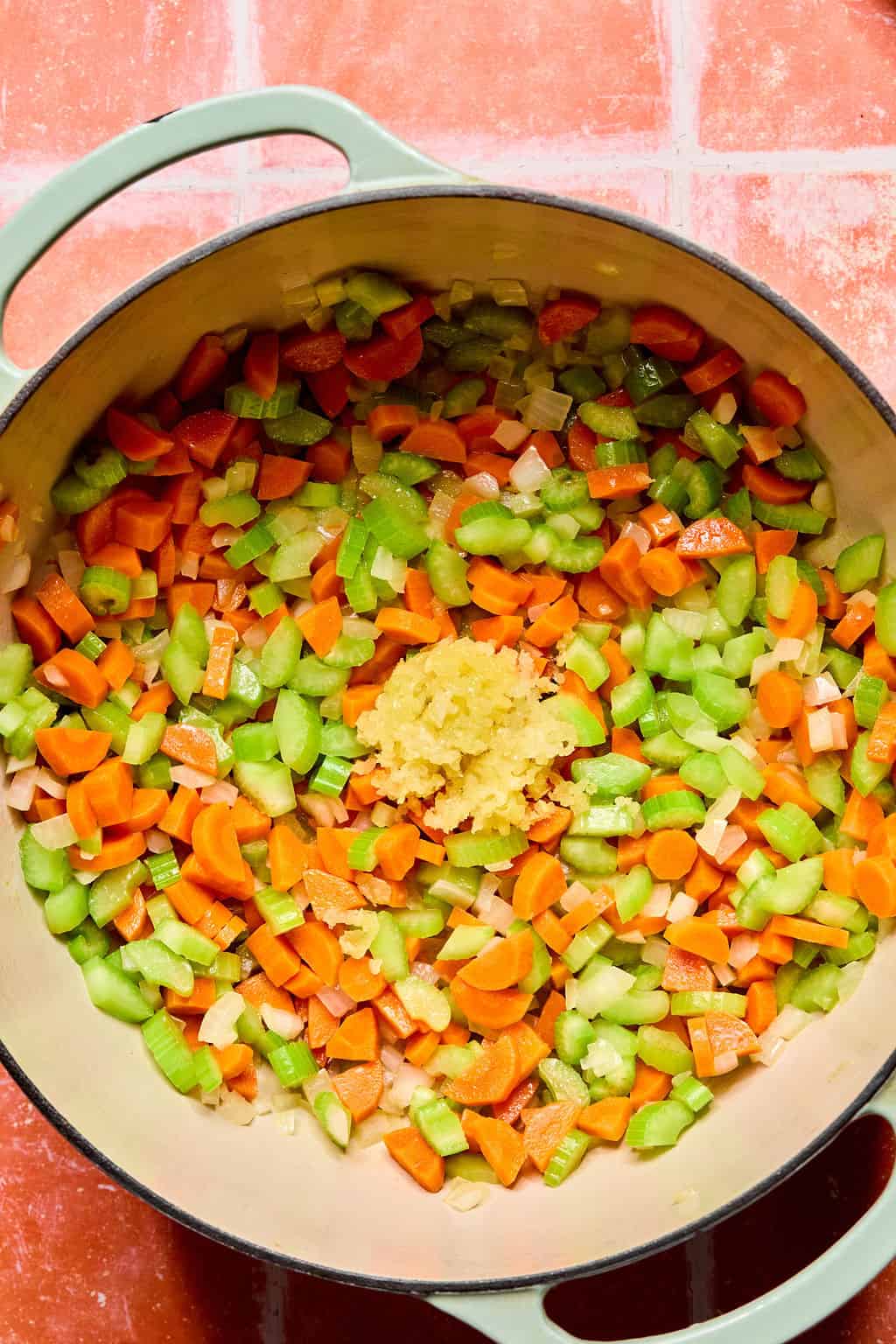 Large Dutch oven with cut up onion, carrots and celery mixed together and garlic added.