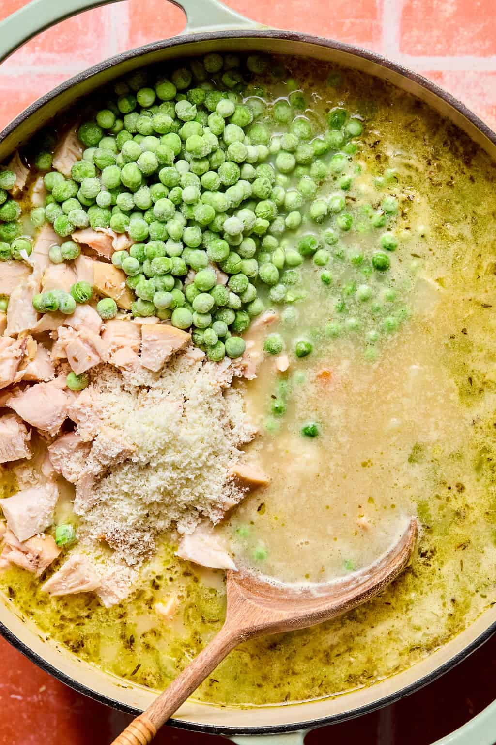 Adding cooked chicken, peas and parmesan cheese to large Dutch oven.