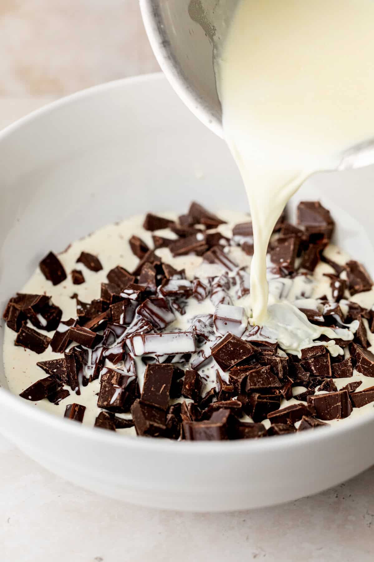 Pouring heavy cream over chocolate in bowl.