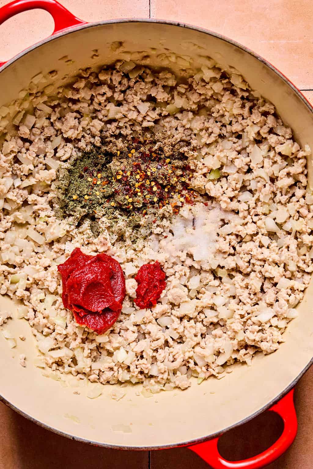 Large Dutch oven with calabrian chili paste, tomato paste, salt, pepper, dried basil, and red pepper flake added.
