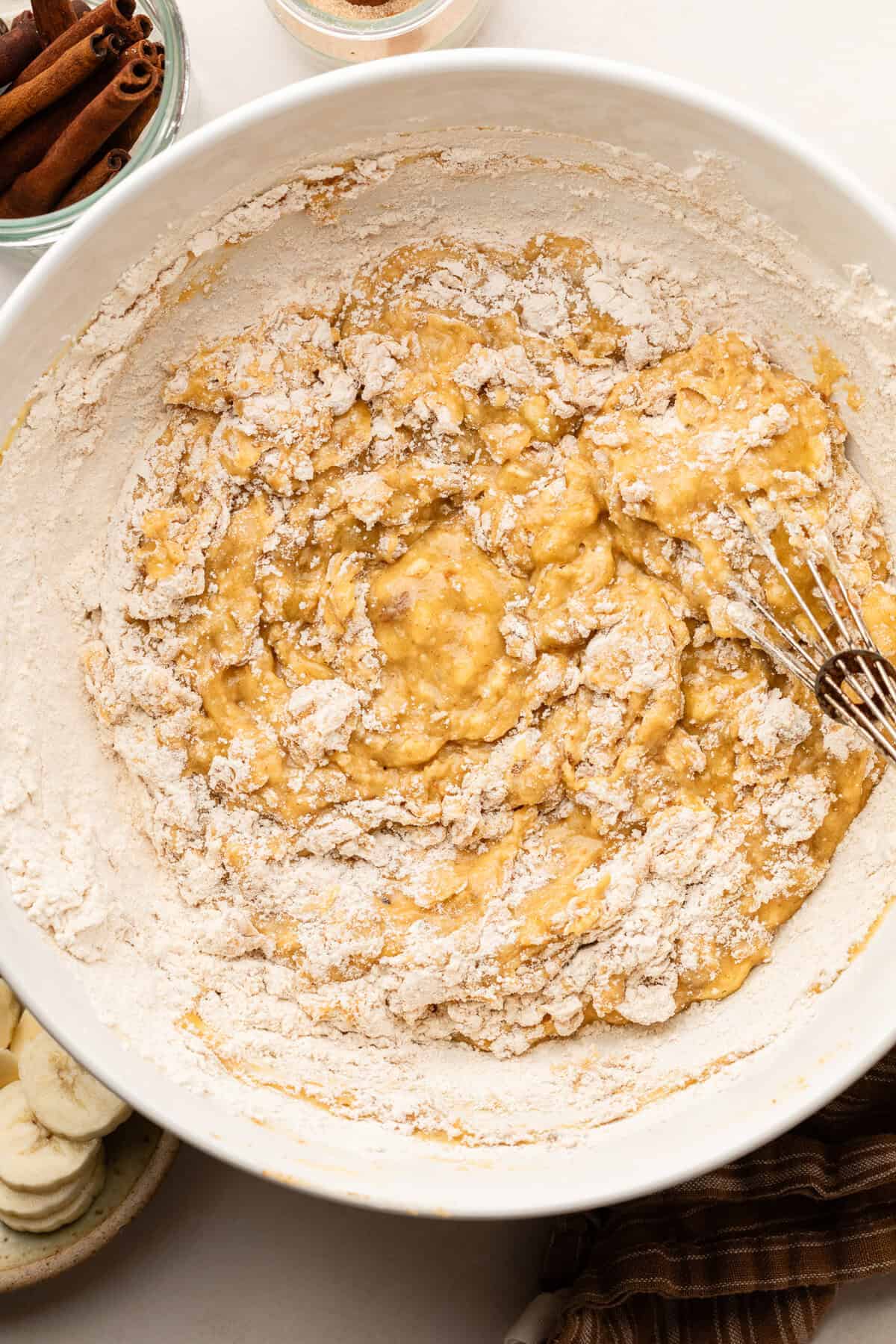 Adding dry ingredients into batter in white bowl.
