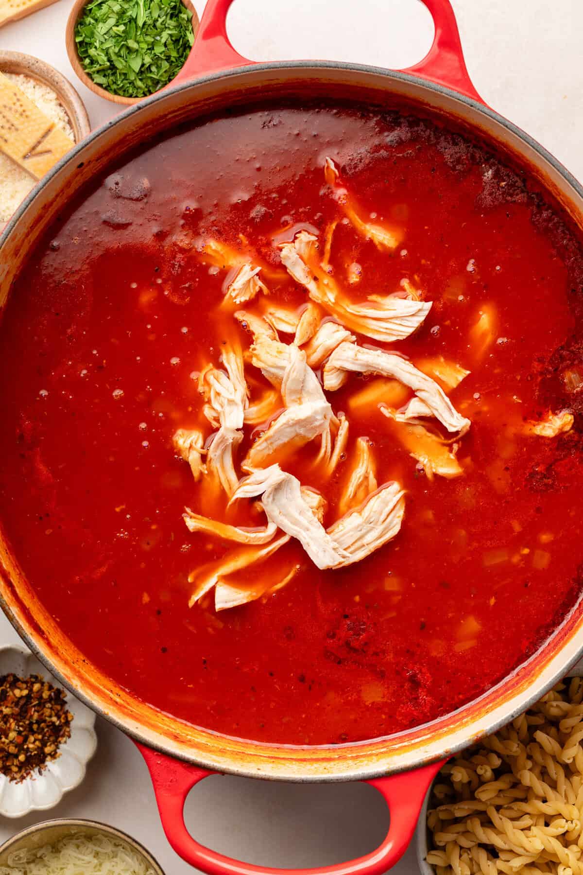red sauce pot with red sauce inside and shredded chicken