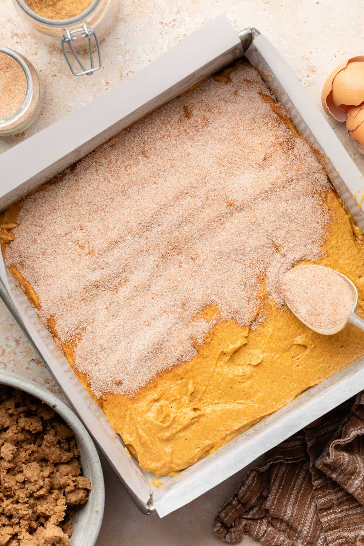 sprinkling cinnamon sugar on top of pumpkin coffee cake batter